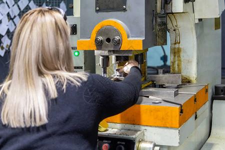 一位长头发的金发女郎在金属加工厂使用机械冲压机工作选择图片素材